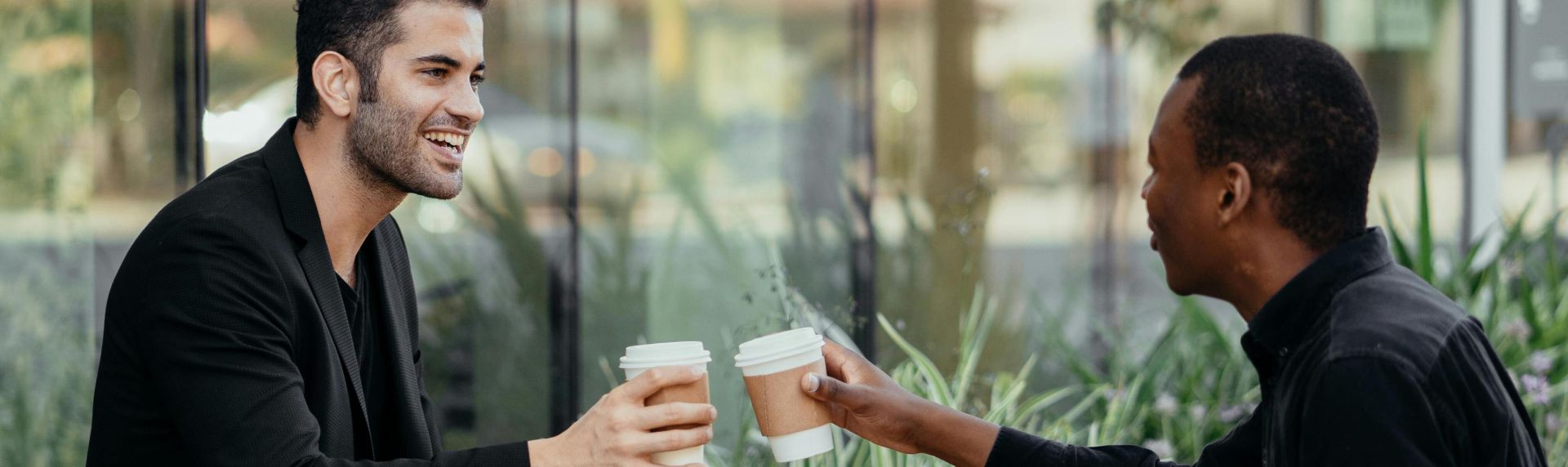 Two men enjoying coffee and conversation outdoors at a casual café setting.