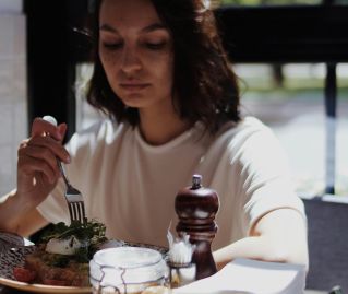 A woman seated alone enjoying a meal in a sunlit café, reflecting tranquility.
