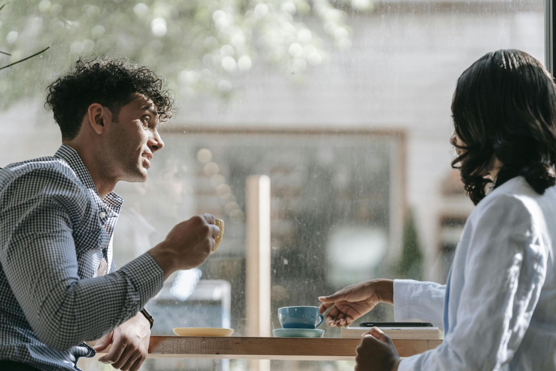 Two adults enjoying a casual conversation over coffee in a cozy café with natural lighting.